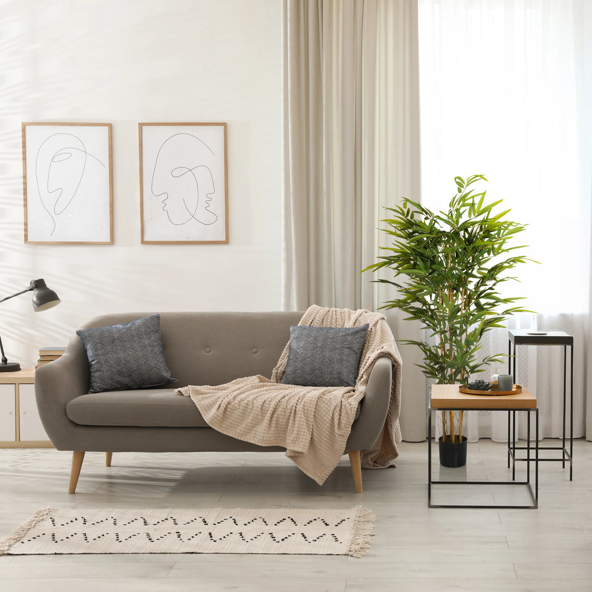 Grøn kunstige plante BAMBUS II i en sort potte ved siden af en sofa fra hjh OFFICE