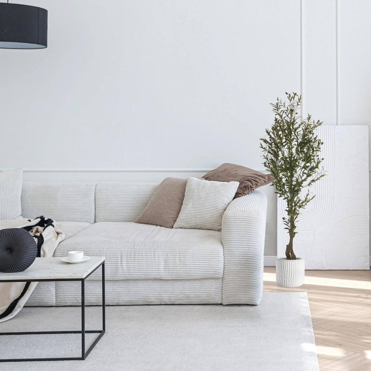 Grøn kunstig plante OLIVE I i en hvid potte ved siden af en lys sofa fra hjh OFFICE