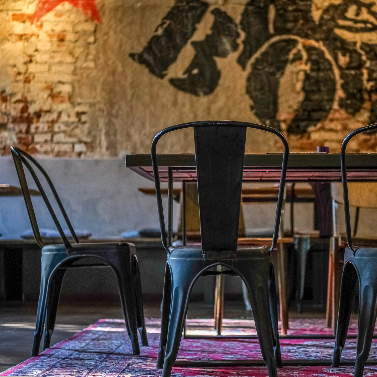 Bagsiden af en sort VANTAGGIO BRUSH bistrostol i metal ved et bord fra hjh OFFICE