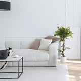 Grøn kunstige plante FICUS I i en hvid potte ved siden af en sofa fra hjh OFFICE